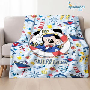 Op de afbeelding: Een lichtblauwe deken met een nautisch thema, met cartoonafbeeldingen van Mickey Mouse in een kapiteunsuniform, schepen, ankers en zeeleven. De deken heeft de naam "William" erop gedrukt.