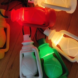 May include: A collection of colorful lantern-shaped string lights. The lanterns are in various colors, including yellow, red, white, and green, and are illuminated. The lights are arranged on a wooden surface.