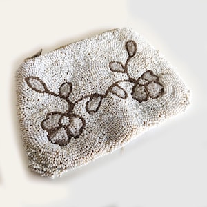 May include: An off-white beaded clutch bag with a floral pattern. The bag is covered in small, round beads. The floral design is in a dark brown colour, with flowers and stems. It has a zip closure.
