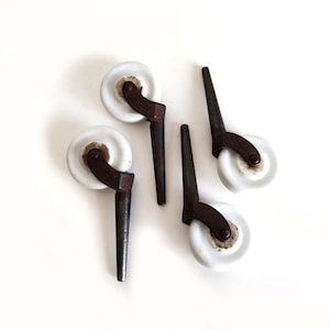 May include: Four antique furniture castors. Each castor features a white ceramic wheel, a dark brown metal bracket, and a dark brown metal stem. The castors are arranged on a white surface.