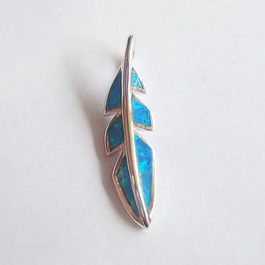 May include: A silver feather pendant with a blue opal inlay. The feather is detailed with a delicate outline and a smooth, polished finish.