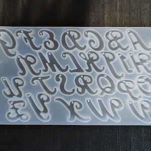 May include: A clear plastic mold with the letters of the alphabet in a cursive font. The mold is designed for creating resin crafts.