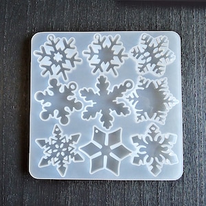 May include: A white silicone mold with nine snowflake shapes. The mold is designed for making resin crafts.