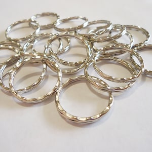May include: A collection of silver-colored, textured metal rings. The rings are oval-shaped with a hammered or ridged surface, and are scattered across a white background. The rings are likely jewelry components or craft supplies.