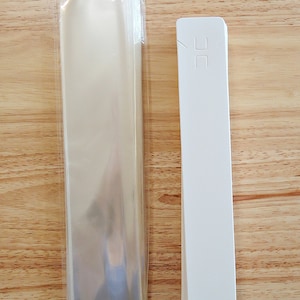 May include: A stack of clear plastic bags and a stack of white paper bags with a small hole in the top.