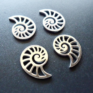 May include: Four silver metal charms shaped like seashells with a spiral design.