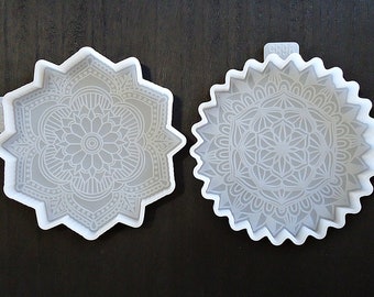 May include: Two white silicone molds with intricate mandala designs. The molds are shaped like stars and have a raised edge.