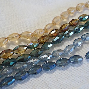 May include: A strand of oval-shaped glass beads in shades of blue, brown, and beige. The beads are faceted and have a shimmery finish.
