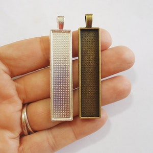 May include: Two rectangular metal pendant trays, one silver and one bronze, with a textured surface. The trays are designed for use with resin or other crafting materials.