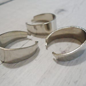 May include: Three silver-toned metal jewelry bails with a smooth, polished finish. Each piece features a C-shaped design with small, inward-facing tabs at the open ends, intended for attaching pendants or charms to necklaces or bracelets.