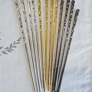 Pu&ograve; includere: Un assortimento di bacchette metalliche in argento, oro e grigio scuro. Le bacchette presentano un design a spirale nella parte superiore e sono disposte su un tessuto bianco. Ideali per la cucina asiatica.