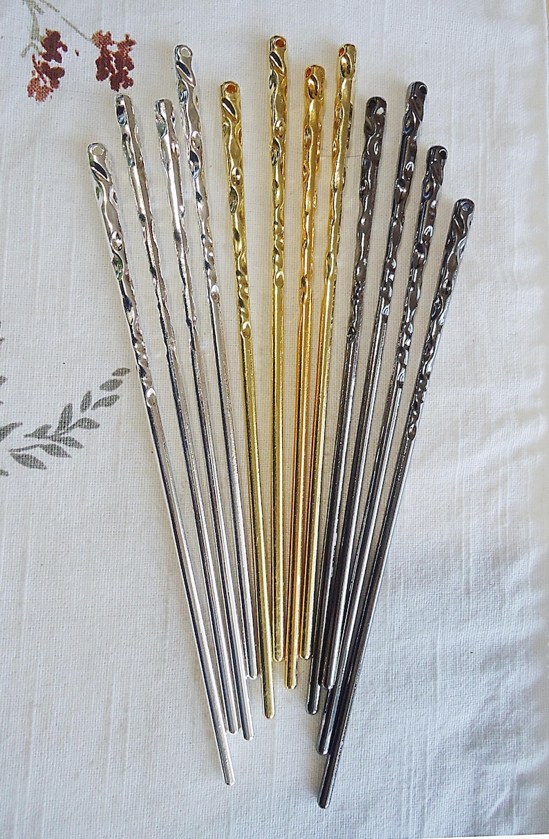 Pu&ograve; includere: Un assortimento di bacchette metalliche in argento, oro e grigio scuro. Le bacchette presentano un design a spirale nella parte superiore e sono disposte su un tessuto bianco. Ideali per la cucina asiatica.