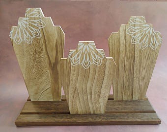 May include: Wooden necklace display stand with three slots. Each slot has a white floral design. The stand is made of natural wood with a brown finish.