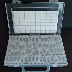May include: A clear plastic storage box with a hinged lid and a handle. The box has 100 small compartments for organizing small items.