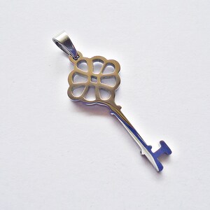 May include: A silver key charm with a decorative flower-shaped head. The key has a simple, straight shaft and a small, rounded handle.
