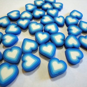May include: A collection of blue and white heart-shaped beads. The hearts have a white center and a blue border with a light blue ring in between.