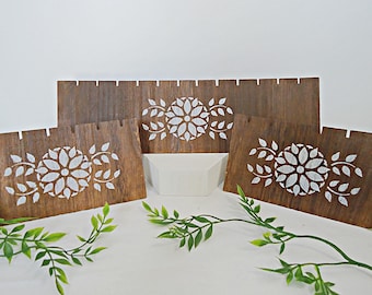 May include: Three wooden plaques with a white floral design. The plaques are made of wood with a brown stain and have a white floral design with leaves.