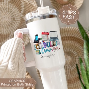 May include: White tumbler with a handle, featuring a colorful "Scheduling Crew" design with a phone, calendar, and laptop. The tumbler includes the name "Jennifer" and a straw. The image also includes the text "Graphics Printed on Both Sides."