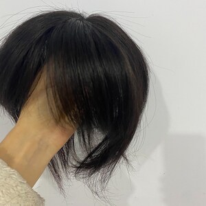 May include: A dark brown hair topper with a layered style. The hairpiece appears to be made of human hair and is designed to add volume and coverage. The hair is styled with a slight wave and a natural-looking part.