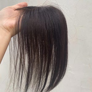 May include: A dark brown hair topper featuring straight, fine strands with a natural sheen. The hairpiece is designed with a base that allows for a smooth, layered appearance, showcasing individual strands that fall vertically in a sleek style.