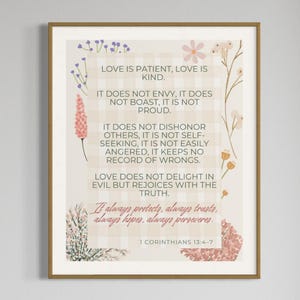 Puede incluir: Una impresión enmarcada con borde dorado presenta el texto "El amor es paciente, el amor es amable" y otras citas inspiradoras de 1 Corintios 13:4-7. El fondo es de color beige claro con detalles florales y a cuadros.