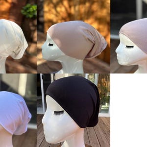 May include: A collection of head coverings in various colors, including white, tan, mauve, light blue, and black. Each head covering is displayed on a white mannequin head, showcasing the fabric's drape and fit. The background is blurred.