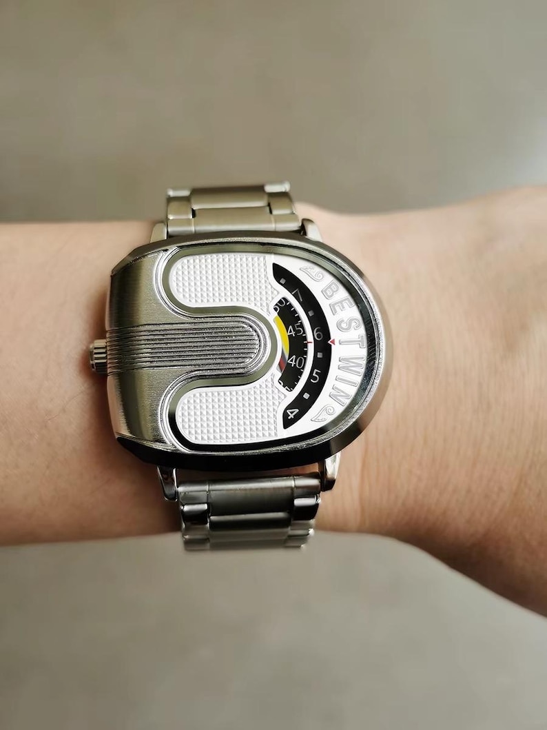 May include: A silver-toned wristwatch with a metallic link band and a unique U-shaped case. The watch face features a textured white surface, a black curved display with the text BESTWIN, and a yellow and red indicator for timekeeping.