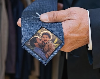 May include: A navy blue tie with a textured pattern. The tie features a personalized photo of a father and child. The tie is held by a person wearing a dark suit. The tie is a unique gift idea.