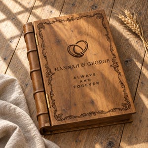 May include: A rectangular wooden book-style box with a hinged spine featuring five raised bands. The cover is engraved with a decorative border, two interlocking rings, the names "HANNAH & GEORGE," and the text "ALWAYS AND FOREVER."