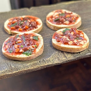 May include: Four small, round, toasted bread slices topped with a red sauce and diced vegetables. The bread slices are arranged on a wooden surface.