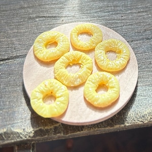 May include: Six yellow pineapple rings on a wooden plate. The rings are arranged in a circle with the largest ring in the centre.