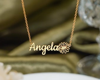 Könnte beinhalten: Eine goldfarbene Halskette mit einer feinen Kette und einem Namensanhänger, der den Namen Angela in Schreibschrift zeigt, ergänzt durch ein kleines, stilisiertes Blumensymbol am Ende des Namens.