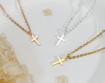 Könnte beinhalten: Drei zarte Halsketten mit kleinen, schlichten Kreuzanhängern. Eine Kette ist roségoldfarben, eine silberfarben und eine goldfarben. Jeder Anhänger hängt an einer passenden dünnen Metallkette mit kleinen, gleichmäßigen, runden Kettengliedern.