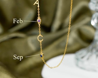 Könnte beinhalten: Eine goldfarbene Kette mit einer vertikalen Anordnung des Buchstabens A, einem violetten runden Edelstein mit der Beschriftung Feb, dem Buchstaben C und einem blauen runden Edelstein mit der Beschriftung Sep. Feine Kettenglieder verbinden die Elemente.