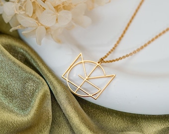 Könnte beinhalten: Eine goldfarbene Halskette mit einem geometrischen Anhänger in Form eines stilisierten Katzenkopfes. Der Anhänger besteht aus dünnen Metalllinien, die eine kreisförmige und dreieckige Kontur mit internen linearen Details bilden. Die Kette ist fein.