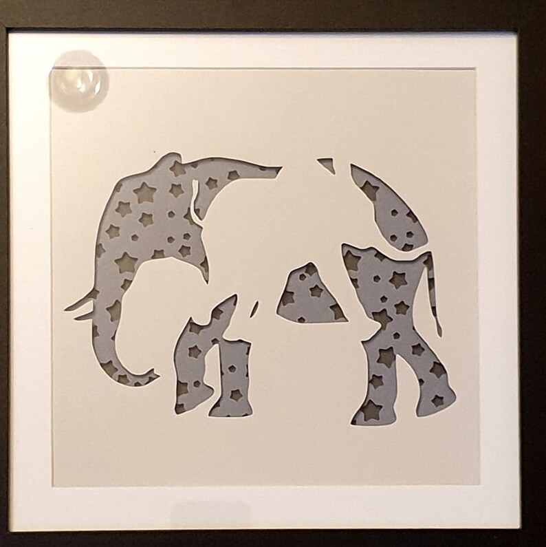 May include: A white paper cutout of two elephants, one standing behind the other, against a background of grey stars.