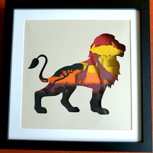 May include: A paper cut-out of a lion with a sunset and African savanna scene inside the silhouette. The lion is black, the sunset is orange, yellow, and red, and the savanna is green and brown.