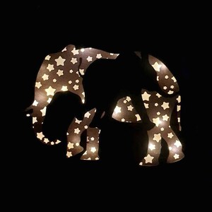 May include: A black silhouette of an elephant with a white star pattern. The elephant is illuminated from behind, creating a glowing effect.