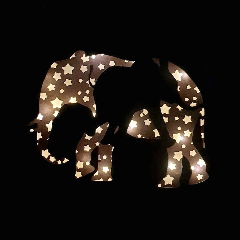 May include: A black silhouette of an elephant with a white star pattern. The elephant is illuminated from behind, creating a glowing effect.