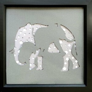 May include: A grey framed picture with a white silhouette of two elephants cut out of the background. The elephants are covered in white stars.
