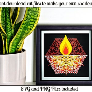 Puede incluir: Un marco de caja de sombra negro con un diseño de papel cortado en rojo, amarillo y blanco de un diya, una lámpara de aceite tradicional india, con el texto "SVG and PNG Files included".