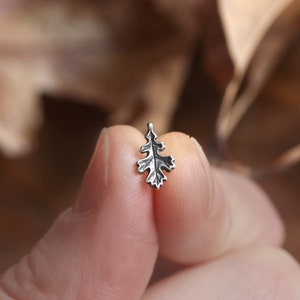 May include: A silver oak leaf charm, held between two fingers, with a detailed design.