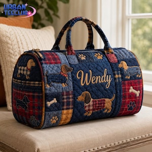 May include: A quilted duffel bag featuring a patchwork design of denim and red plaid fabric. The bag is decorated with embroidered dachshund dogs, paw prints, and bones. The name Wendy is embroidered in gold script on the side of the bag.