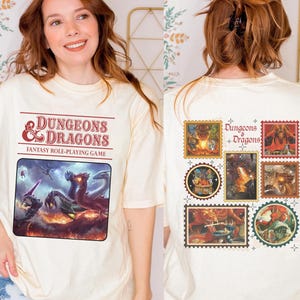 May include: Cream-colored t-shirt featuring the text "Dungeons & Dragons Fantasy Role-Playing Game" in red. The front graphic shows a fantasy scene with dragons. The back of the shirt has several postage stamp-style graphics with D&D imagery.