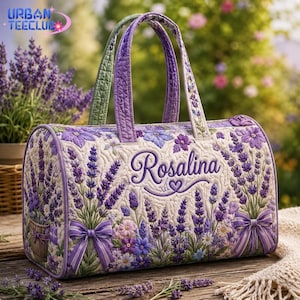 May include: A quilted duffel bag featuring a lavender floral pattern with purple bows and the name Rosalina embroidered in script. The bag has two purple handles and a light-colored background with detailed stitching throughout the fabric.