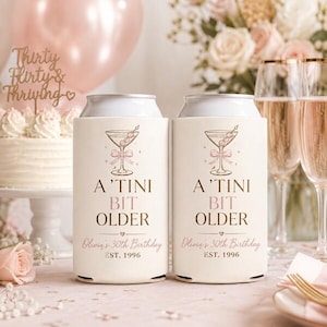 May include: Two white can coolers with a martini glass design and the text "A 'TINI BIT OLDER" in a script font. The coolers are personalized with "Olivia's 30th Birthday" and "EST. 1996". The background includes a cake and champagne flutes.