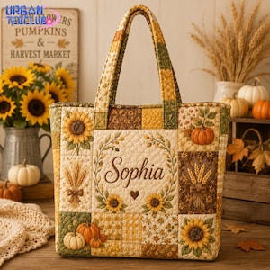 May include: A quilted tote bag featuring a patchwork design of sunflowers, pumpkins, and wheat stalks in shades of yellow, orange, and brown. The center panel displays the name Sophia in cursive script surrounded by a floral and wheat wreath.