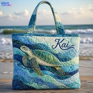 May include: A quilted tote bag featuring a sea turtle swimming through blue and green waves. The fabric has a textured, stitched pattern throughout. The name Kai is embroidered in dark blue script on the upper right side of the bag.