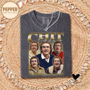 May include: Dark gray t-shirt with a gold-colored "CHIT" graphic and multiple images of a man wearing glasses. The text "Do It Lady" is below the main graphic. A silver chain necklace is draped across the shirt.