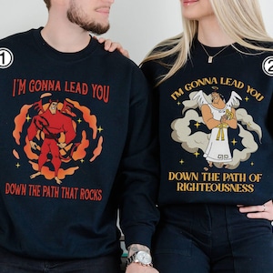 May include: Two navy blue sweatshirts with matching graphics. One features a red cartoon figure in a fiery design with the text "I'M GONNA LEAD YOU DOWN THE PATH THAT ROCKS." The other has an angel with the text "I'M GONNA LEAD YOU DOWN THE PATH OF RIGHTEOUSNESS."